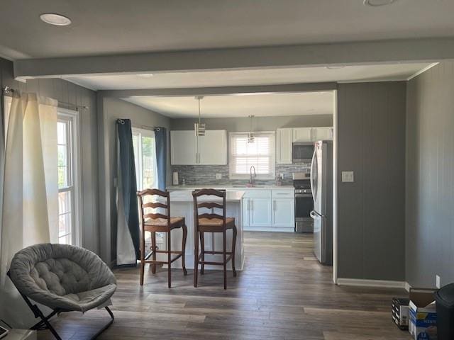 kitchen featuring appliances with stainless steel finishes, light countertops, white cabinets, a breakfast bar, and dark wood-type flooring