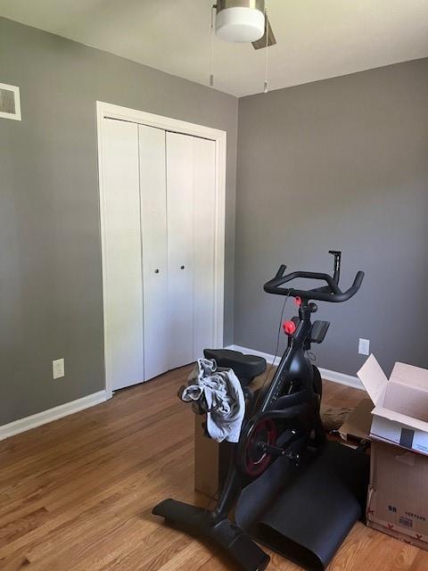 exercise area featuring baseboards, a ceiling fan, wood finished floors, and visible vents