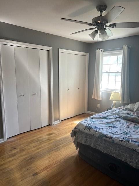 bedroom featuring baseboards, multiple closets, ceiling fan, and light wood-type flooring