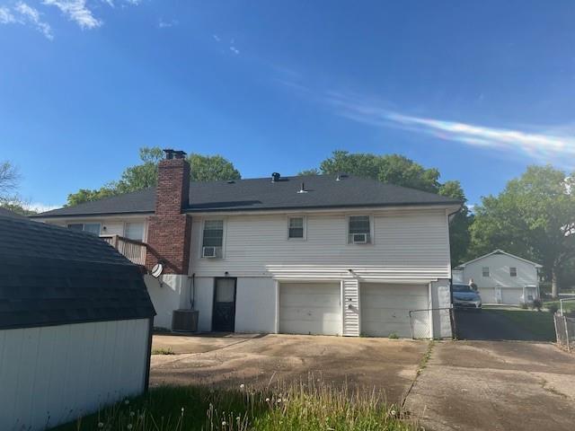 back of house with an attached garage, driveway, and a chimney