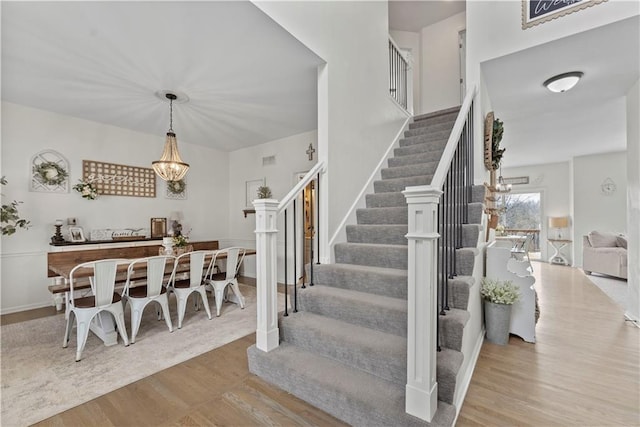 stairway with baseboards, a notable chandelier, and wood finished floors