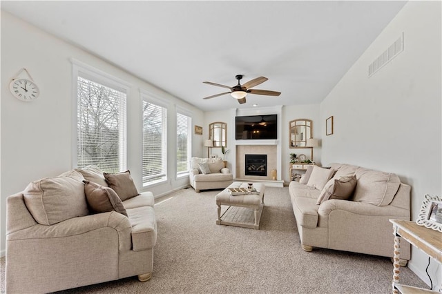living area with carpet floors, a ceiling fan, visible vents, and a glass covered fireplace