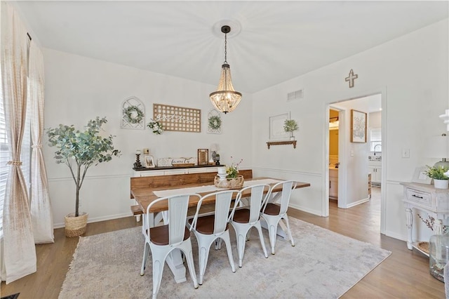 dining space featuring baseboards, visible vents, light wood-style flooring, and a notable chandelier