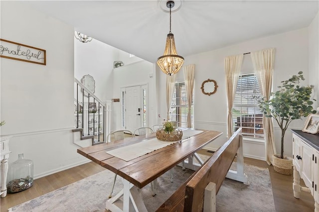 dining space featuring baseboards, wood finished floors, a chandelier, and stairway