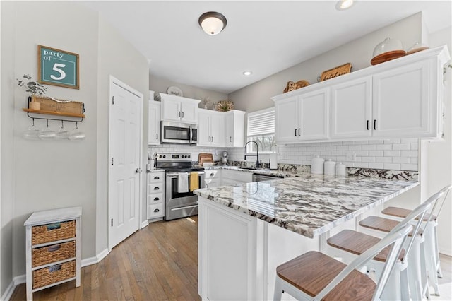 kitchen with light stone counters, white cabinets, a peninsula, stainless steel appliances, and hardwood / wood-style floors