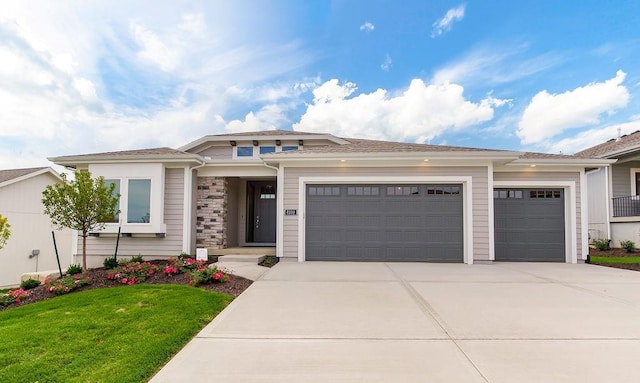 prairie-style house with a garage, driveway, a front yard, and stone siding