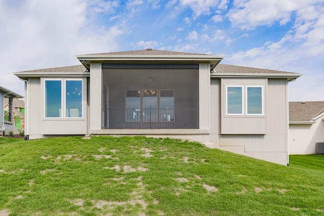rear view of property featuring a lawn, a sunroom, central AC, and roof with shingles