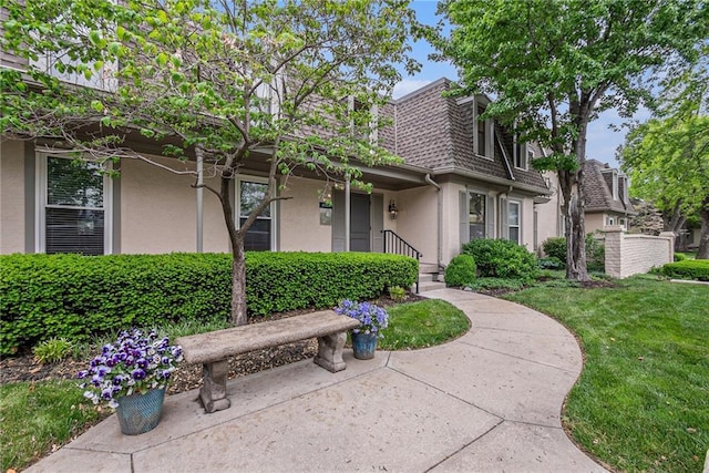 view of front of home featuring a shingled roof, stucco siding, mansard roof, and a front lawn
