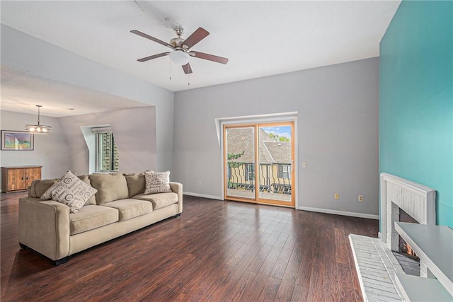 living room featuring baseboards, a brick fireplace, ceiling fan with notable chandelier, and wood finished floors