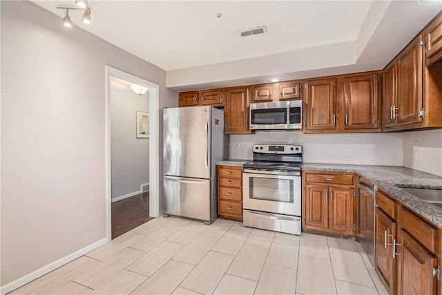 kitchen featuring appliances with stainless steel finishes, brown cabinets, and visible vents