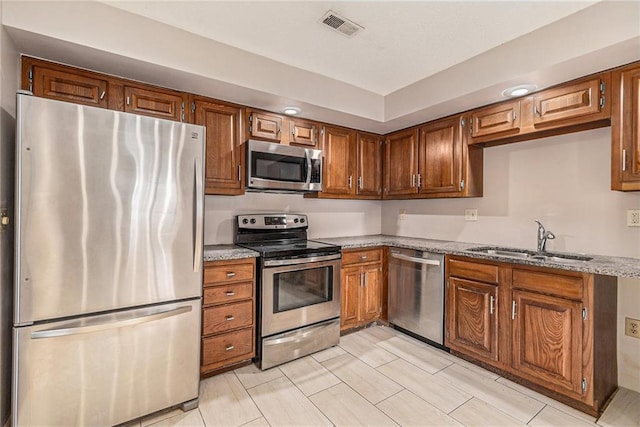 kitchen featuring appliances with stainless steel finishes, light stone counters, a sink, brown cabinetry, and visible vents