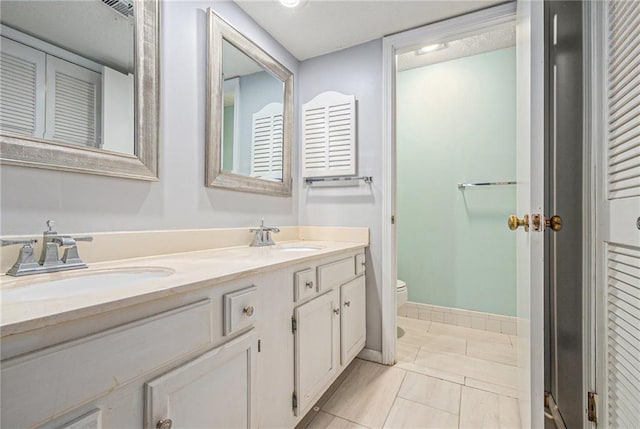 full bathroom featuring double vanity, a sink, baseboards, and toilet