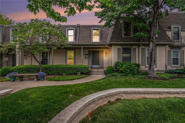 multi unit property with a shingled roof, stucco siding, mansard roof, and a front yard