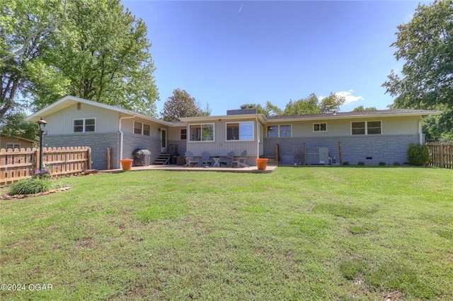 rear view of house with fence, stone siding, cooling unit, a patio area, and a yard