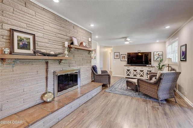 living area featuring ornamental molding, wood finished floors, baseboards, a stone fireplace, and a textured ceiling