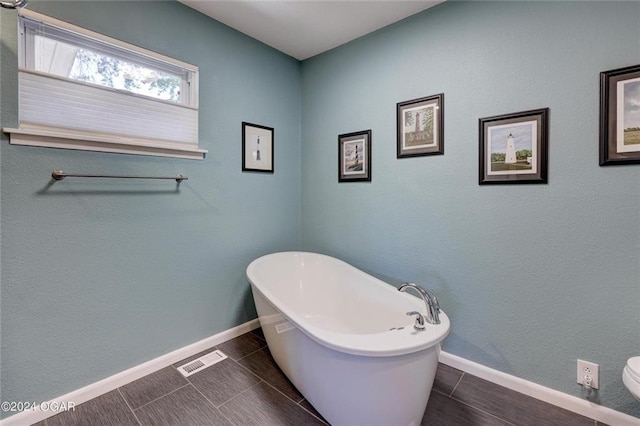 bathroom featuring toilet, a freestanding tub, visible vents, and baseboards
