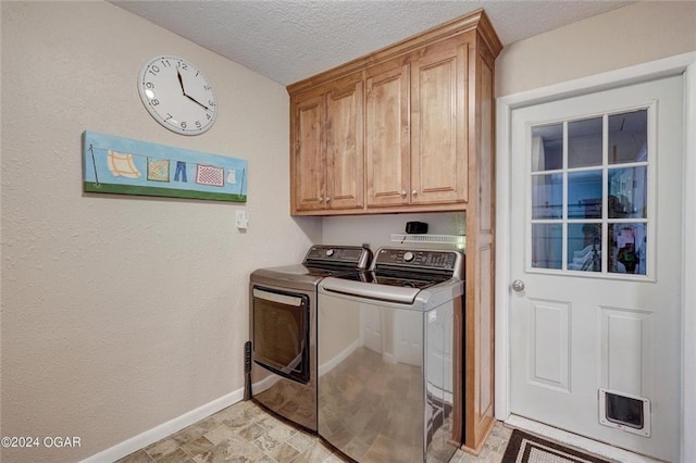 clothes washing area with cabinet space, a textured ceiling, baseboards, and washer and clothes dryer