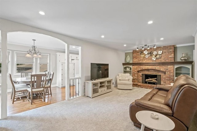 living area featuring carpet floors, a brick fireplace, a chandelier, recessed lighting, and ornamental molding