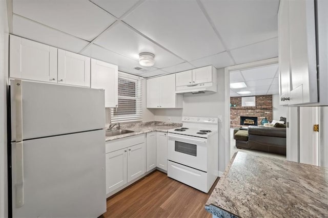 kitchen featuring white appliances, a brick fireplace, a paneled ceiling, white cabinetry, and under cabinet range hood