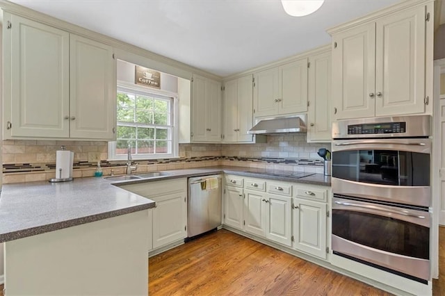 9817 Cedar St, Overland Park, KS 66207 - kitchen featuring appliances with stainless steel finishes, a sink, under cabinet range hood, a peninsula, and backsplash