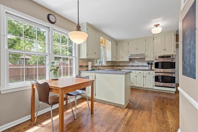 9817 Cedar St, Overland Park, KS 66207 - kitchen featuring stainless steel double oven, under cabinet range hood, dark wood-type flooring, backsplash, and a peninsula