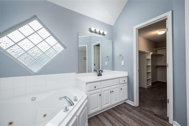 bathroom featuring a walk in closet, vaulted ceiling, a tub with jets, wood finished floors, and vanity