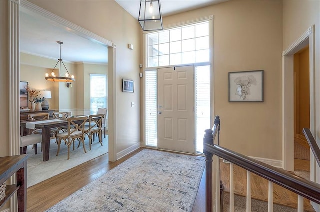 entrance foyer with baseboards, ornamental molding, a chandelier, and wood finished floors