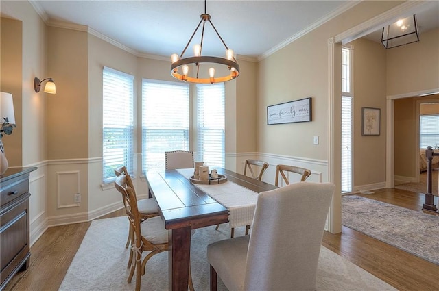 dining area featuring a wainscoted wall, wood finished floors, a healthy amount of sunlight, and a notable chandelier