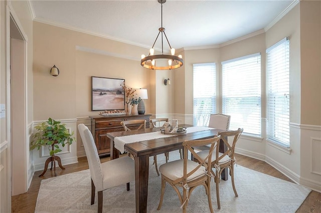 dining space with light wood finished floors, a wainscoted wall, a wealth of natural light, and a chandelier
