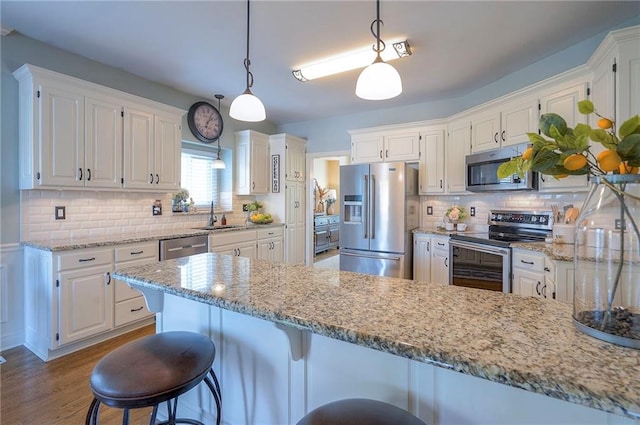 kitchen with light stone countertops, white cabinetry, a peninsula, backsplash, and stainless steel appliances