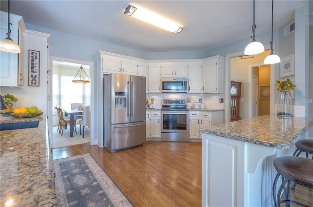 kitchen featuring a breakfast bar area, a sink, dark wood-type flooring, backsplash, and stainless steel appliances