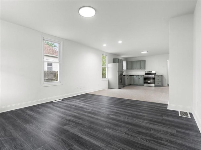 unfurnished living room with baseboards, visible vents, a healthy amount of sunlight, and wood finished floors