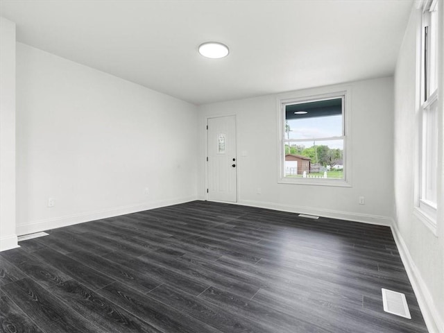 empty room with plenty of natural light, dark wood finished floors, baseboards, and visible vents
