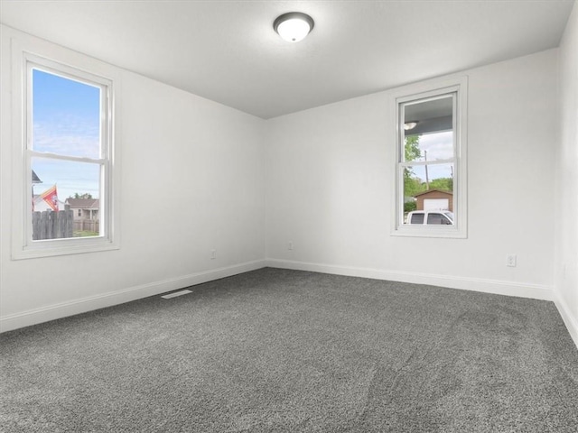 empty room with dark colored carpet, baseboards, and visible vents