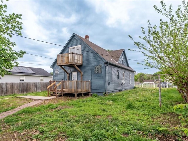 rear view of property featuring fence, a deck, a chimney, a balcony, and a lawn