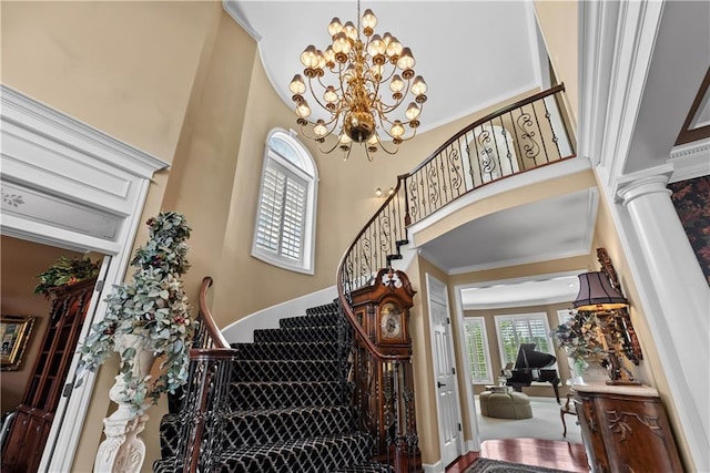 foyer with stairs, a notable chandelier, decorative columns, and a towering ceiling