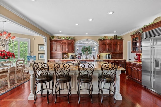 kitchen with light stone counters, backsplash, a kitchen bar, glass insert cabinets, and built in refrigerator