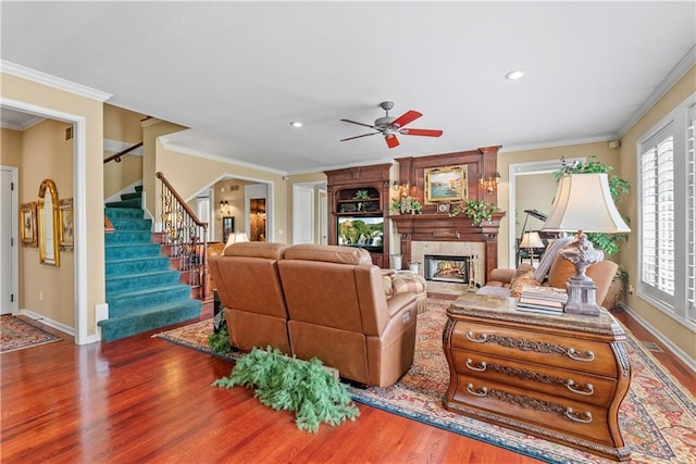 living room with a ceiling fan, baseboards, ornamental molding, stairs, and wood finished floors