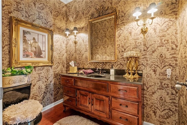 bathroom with vanity, baseboards, wallpapered walls, and wood finished floors