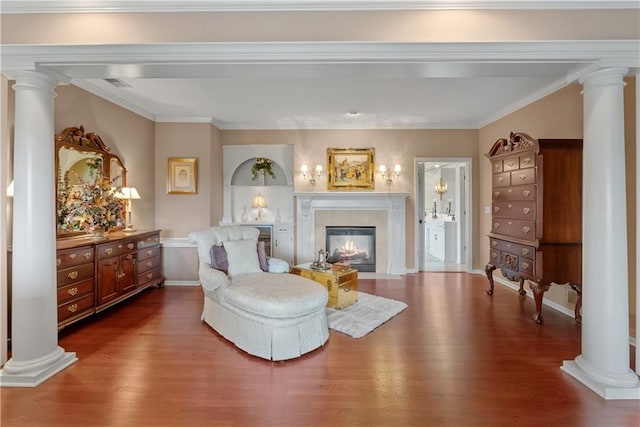 living area featuring wood finished floors, ornamental molding, ornate columns, baseboards, and a tile fireplace