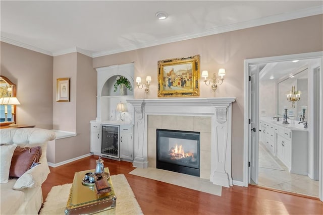 living area featuring a tile fireplace, wood finished floors, baseboards, ornamental molding, and wine cooler