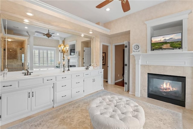 bathroom featuring a tiled fireplace, a sink, ceiling fan with notable chandelier, a shower stall, and double vanity
