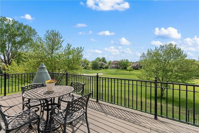 wooden deck with golf course view, a lawn, and outdoor dining space
