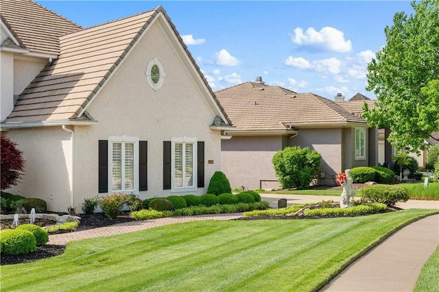 back of property featuring a lawn, stucco siding, and a tile roof