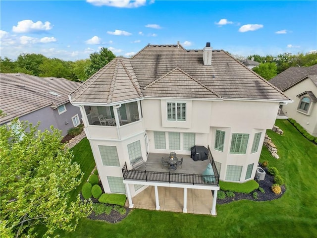 rear view of property with a sunroom, stucco siding, a chimney, and a lawn