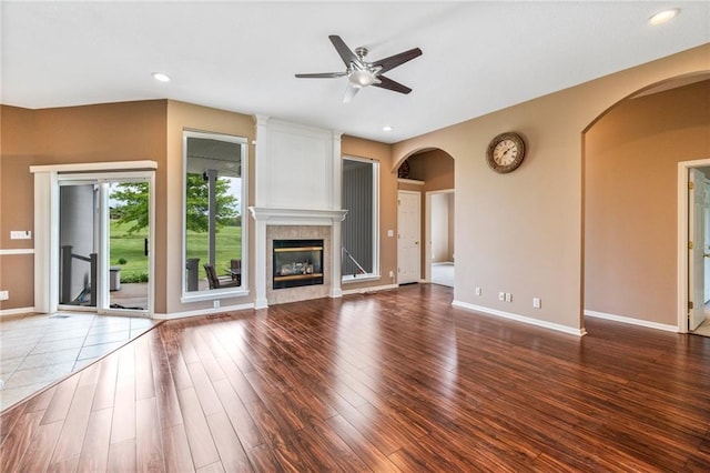 unfurnished living room featuring wood finished floors, baseboards, ceiling fan, a tile fireplace, and arched walkways
