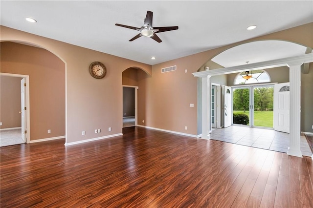 unfurnished living room with ceiling fan, visible vents, arched walkways, wood finished floors, and baseboards