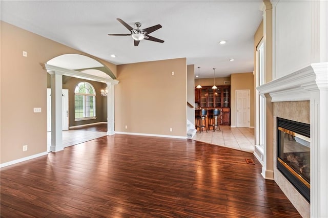 unfurnished living room with ceiling fan, a tiled fireplace, recessed lighting, decorative columns, and wood finished floors