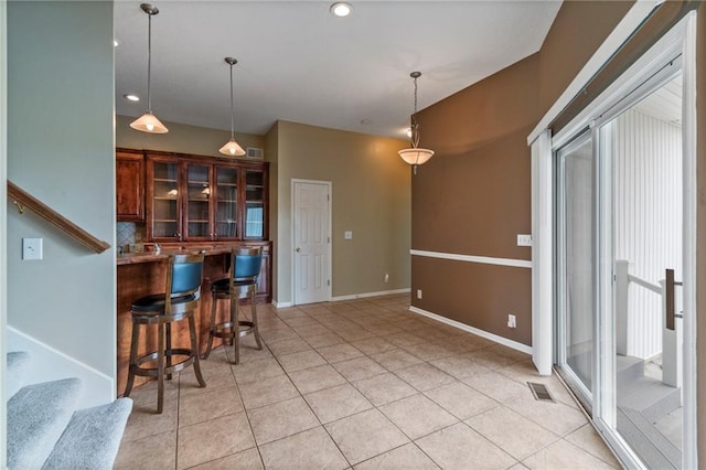 kitchen with hanging light fixtures, light tile patterned floors, a kitchen bar, visible vents, and glass insert cabinets