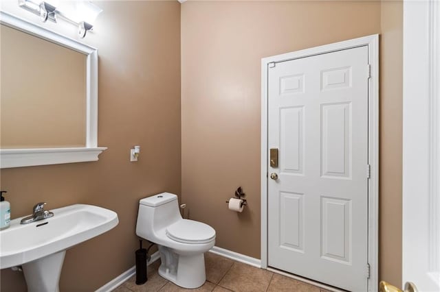 bathroom featuring baseboards, a sink, tile patterned floors, and toilet